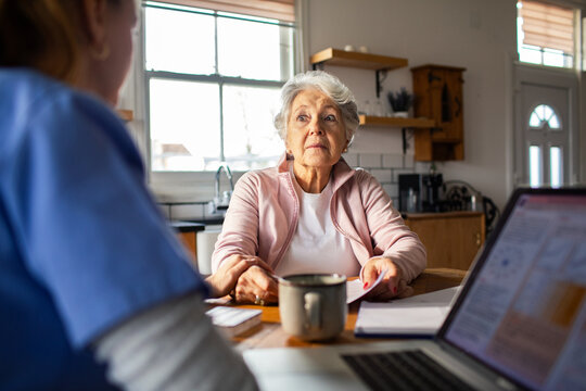 Senior woman consulting home nurse at kitchen table