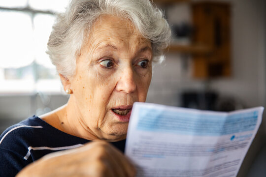 Shocked senior woman reading utility bill at home