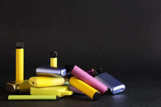 Colorful assortment of electronic cigarettes and vape devices on black background with copy space, group of disposable vapes and refillable e-cigarettes for smoking alternative concept