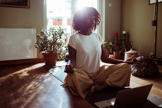 Young woman practicing meditation at home with laptop