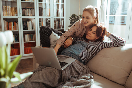 Two women relaxing with laptop on cozy sofa at home