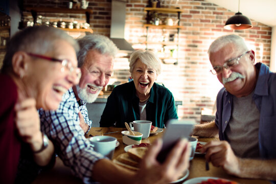 Senior friends laughing at smartphone in home kitchen