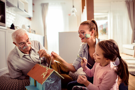 Grandfather, mother and daughter painting a birdhouse at home