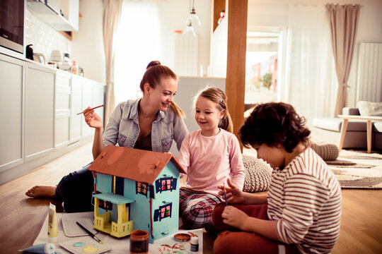 Mother and children painting a dollhouse at home