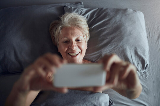 Smiling senior woman taking selfie in bed at home