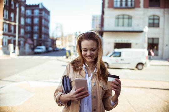 Young woman with coffee using smartphone on city street