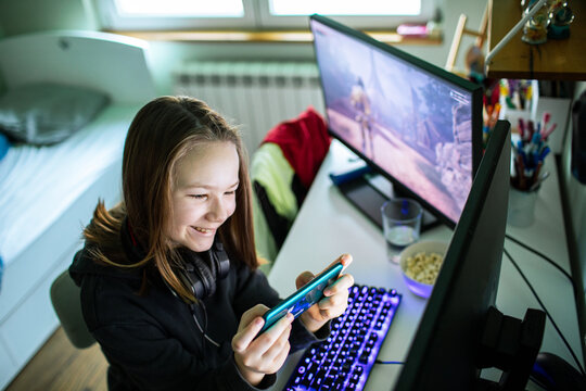 Smiling teenage girl playing mobile game at home desk