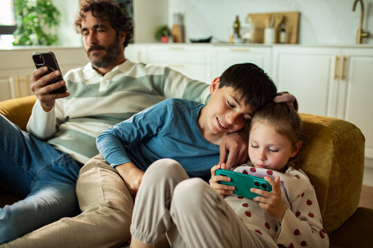 Father and children using smartphones on sofa at home