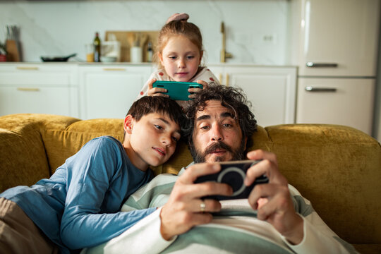 Father and children playing mobile games on living room sofa