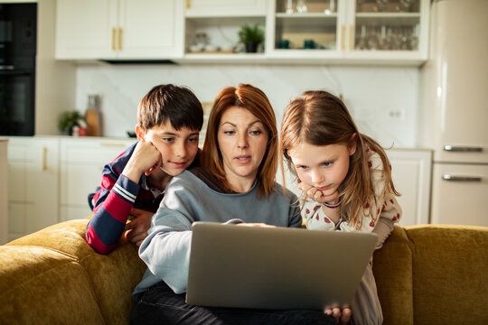 Mom with son and daughter using laptop on sofa at home