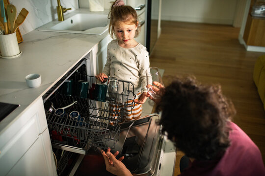 Parent teaching child to load dishwasher in modern kitchen