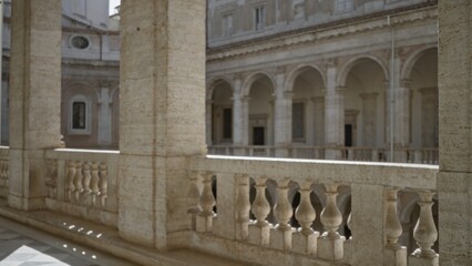 Fototapeta premium Weathered limestone balustrade and fluted columns overlooking a sunlit arched courtyard in soft blurred focus museum; background backplate copyspace calm.