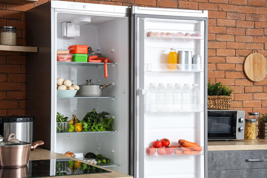 Big modern fridge with fresh products on brown brick background in kitchen