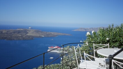 Obraz premium Terrace with white cafe chairs and metal railing in shallow blurred focus overlooking blue sea and distant islands outdoor; background copyspace.