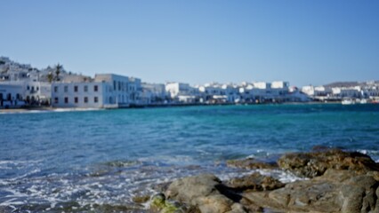 Fototapeta premium Coastal waterfront scene softly defocused bokeh background outdoor showing turquoise sea, blurred white buildings and rocky shore in shallow focus; background copyspace calm.