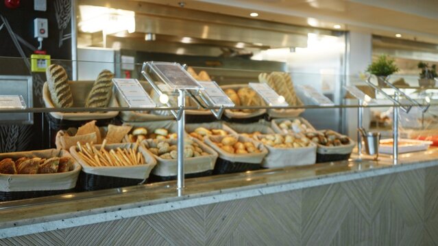 Bakery counter lined with baskets of assorted rolls, breadsticks and loaves in shallow defocused bokeh, shop; backdrop overlay calm.