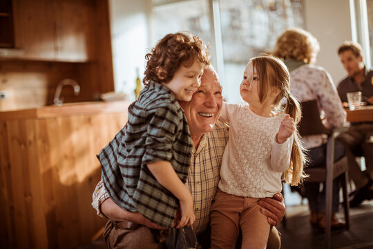 Smiling grandfather hugging grandchildren at home kitchen