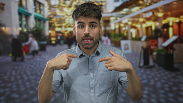Man with tongue out waving hand on busy urban street under evening lights near storefronts; playful greeting.