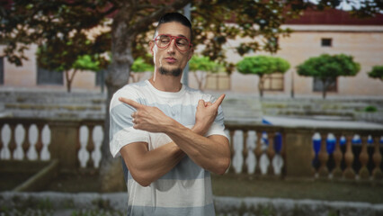 Obraz premium Man in striped t shirt wearing red glasses points finger to chest and looks left in front of building; contemplation urban.