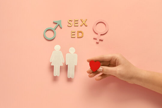 Hand with heart, figures of couple, female and male symbols and text SEX ED on pink background. Sex education