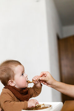 Mother feeding cute baby infant in high chair with complementary food. Family domestic life. Mom and son having dinner together, joyful moment. Happy Mother's day!
