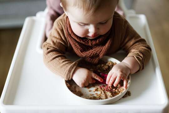 Cute baby infant eating complementary food and trying fruit close up in high chair. Family domestic life. Mom and son having dinner together. blw