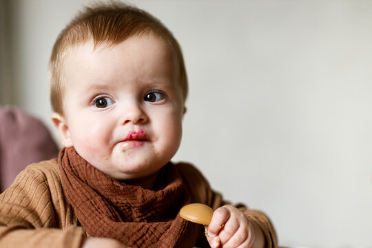 Cute baby infant eating complementary food and trying fruit close up in high chair. Family domestic life. Mom and son having dinner together. blw