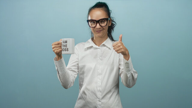 Woman holding a mug that reads iam the boss, wearing white shirt and glasses, showing thumbs up gesture in studio; confidence leadership empowerment.
