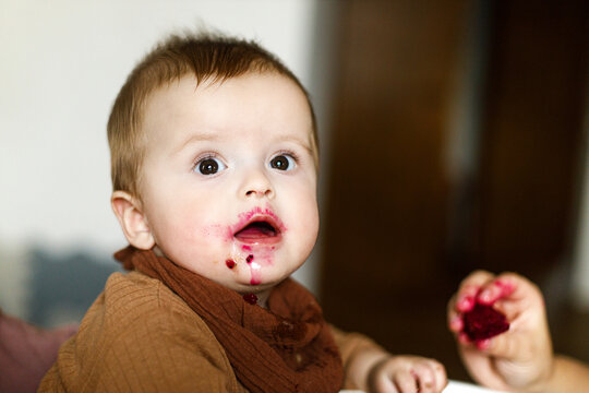 Cute baby infant eating complementary food and trying fruit close up in high chair. Family domestic life. Mom and son having dinner together. blw