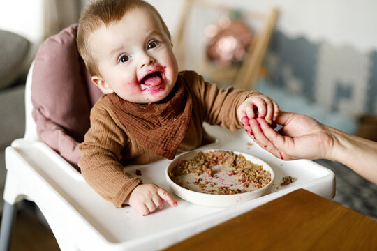Mother feeding cute happy baby infant with fuit close up, eating complementary food. Family domestic life. Mom and son together, joyful moment