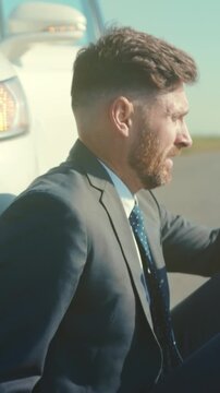 Man in suit beside wrecked vehicle, Tired sales professional in formal clothing pauses by broken down vehicle