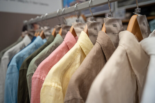 Many colorful linen shirts hanging on hangers at fashion clothing store, new collection of fashion wear items presented in apparel shop, stylish garments on sale, showroom selling designers clothes.