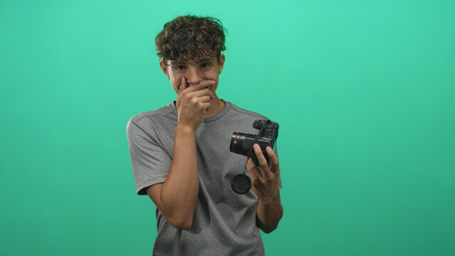 Man holding dslr camera, hand covering mouth and looking down in studio; creative frustration process.