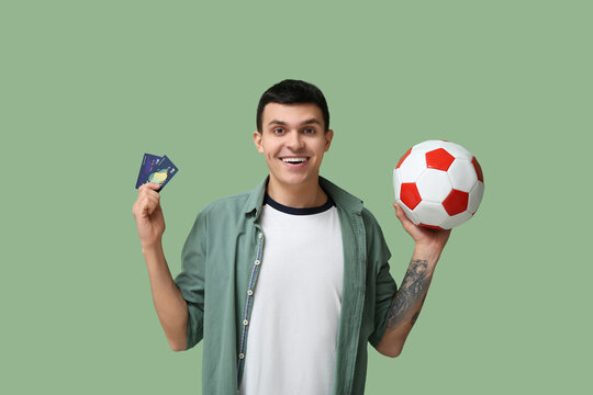Young man with soccer ball and credit cards on green background