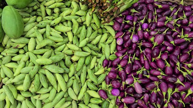 Colorful stack of fresh vegetables in a busy vegetable market. Eggplant, cauliflower, ridge gourd, pointed gourd, bitter melon, tomatoes, spinach, okra, beans, carrots, pumpkins