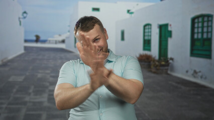 Fototapeta premium Man waving both hands on a sunlit street lined with white buildings and green shutters; joy travel leisure.