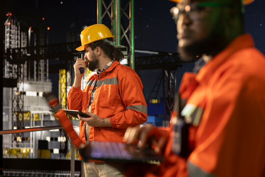 Offshore oil extraction platform team using laptop to control subsea systems late at night. Experts working together to monitor anomaly detection using notebook on drilling derrick