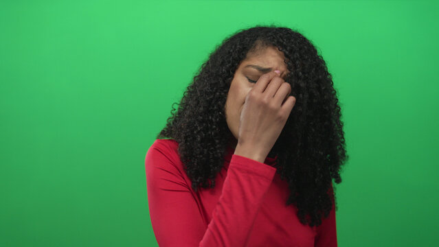 African american woman in red shirt with curly hair pinches nose and closes eyes in studio; disgust reaction.