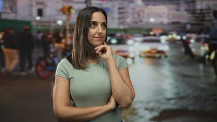 Fototapeta premium Woman hand on chin in a busy urban street with cars, headlights and blurred crowd at night; thoughtful introspection.