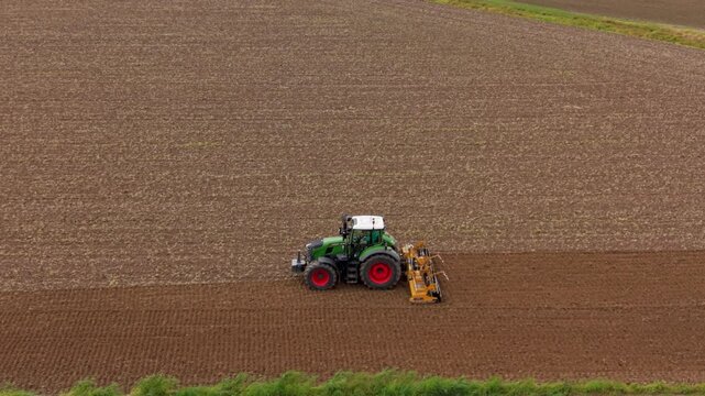 Tractor plowing a field: An agricultural tractor with modern design is actively plowing a large, tilled field, creating neat rows in the soil, under an overcast sky.