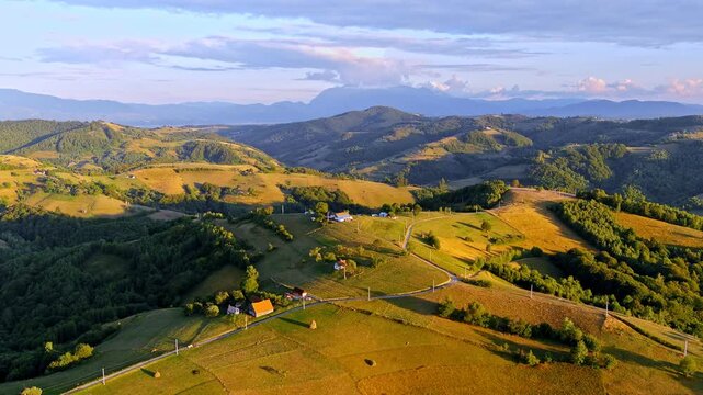 Aerial view of the rolling hills and scattered houses of Transylvania during golden hour in Holbav, Brasov, Romania.