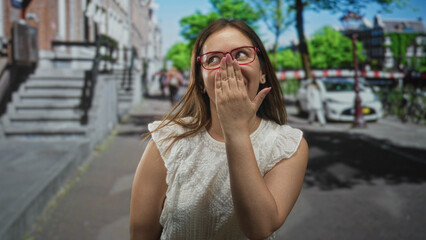 Fototapeta premium Woman hand covering mouth on street in city wearing red glasses and white lace top by stone steps and parked car; shy surprise.