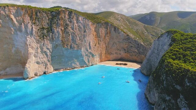 Aerial view of Navagio Beach featuring the famous shipwreck, towering white cliffs, and crystal clear turquoise water with small boats in Elatia, Greece.