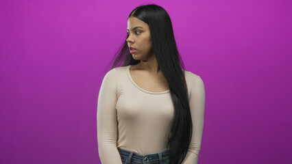 Naklejka premium Young latin woman clutches chest and gazes sideways in studio setting with purple backdrop; anxiety.