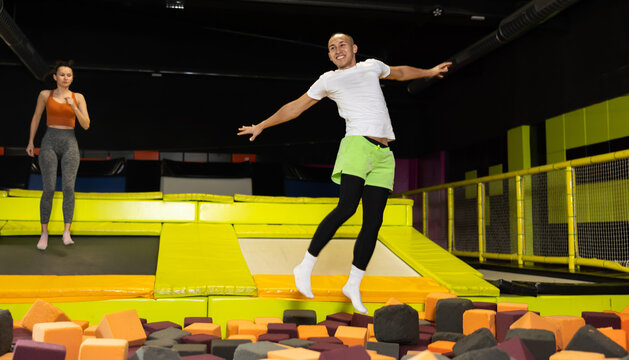 Emotional joyful guy jumping into foam pit at indoor trampoline arena, with friends leaping nearby