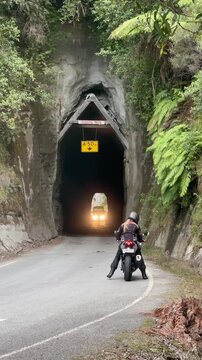 A female motorcyclist stops before entering Hobbit's Hole tunnel in Manawatu-Whanganui, New Zealand, a car approaches from the other side.