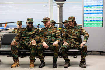 Fototapeta premium Waiting, plane arrival and smiling military team in busy airport lounge. Chatting, airplane departure and cheerful army squad enduring long flight layover in transit hub, passing time