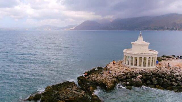 Aerial view of the Lighthouse of Saint Theodore with its circular colonnade on the rocky coast with a person standing on the shore in Argostolion, Greece.