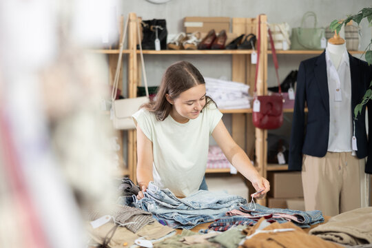 Teenage girl stands near a shelf with clothes and pants and chooses jeans. Schoolchild buys clothes in a store