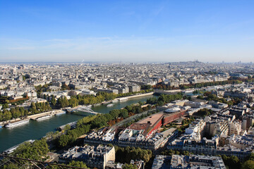 Naklejka premium Wide aerial view of Paris featuring the Seine River, bridges and classic architecture. Scenic panoramic cityscape of the French capital under clear blue sky.